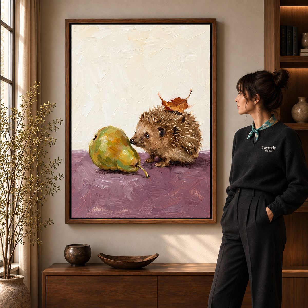 Hedgehog and Pear artwork in a walnut frame beside a standing woman in a warm room.