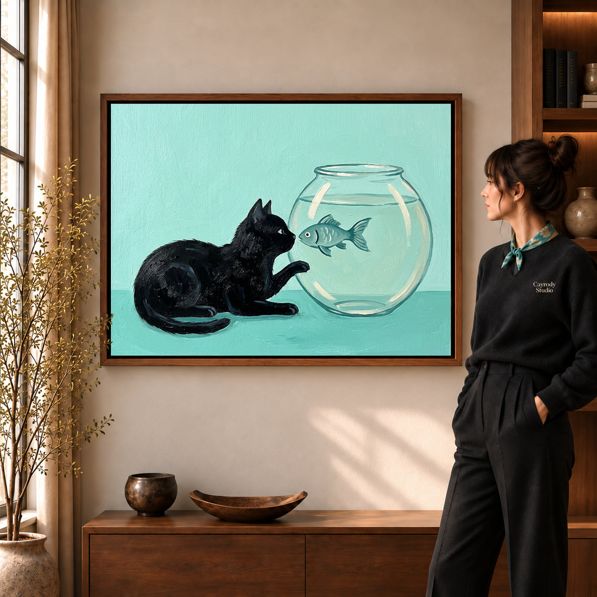 Curious Fishbowl Cat artwork in a walnut frame beside a standing woman in a warm room.