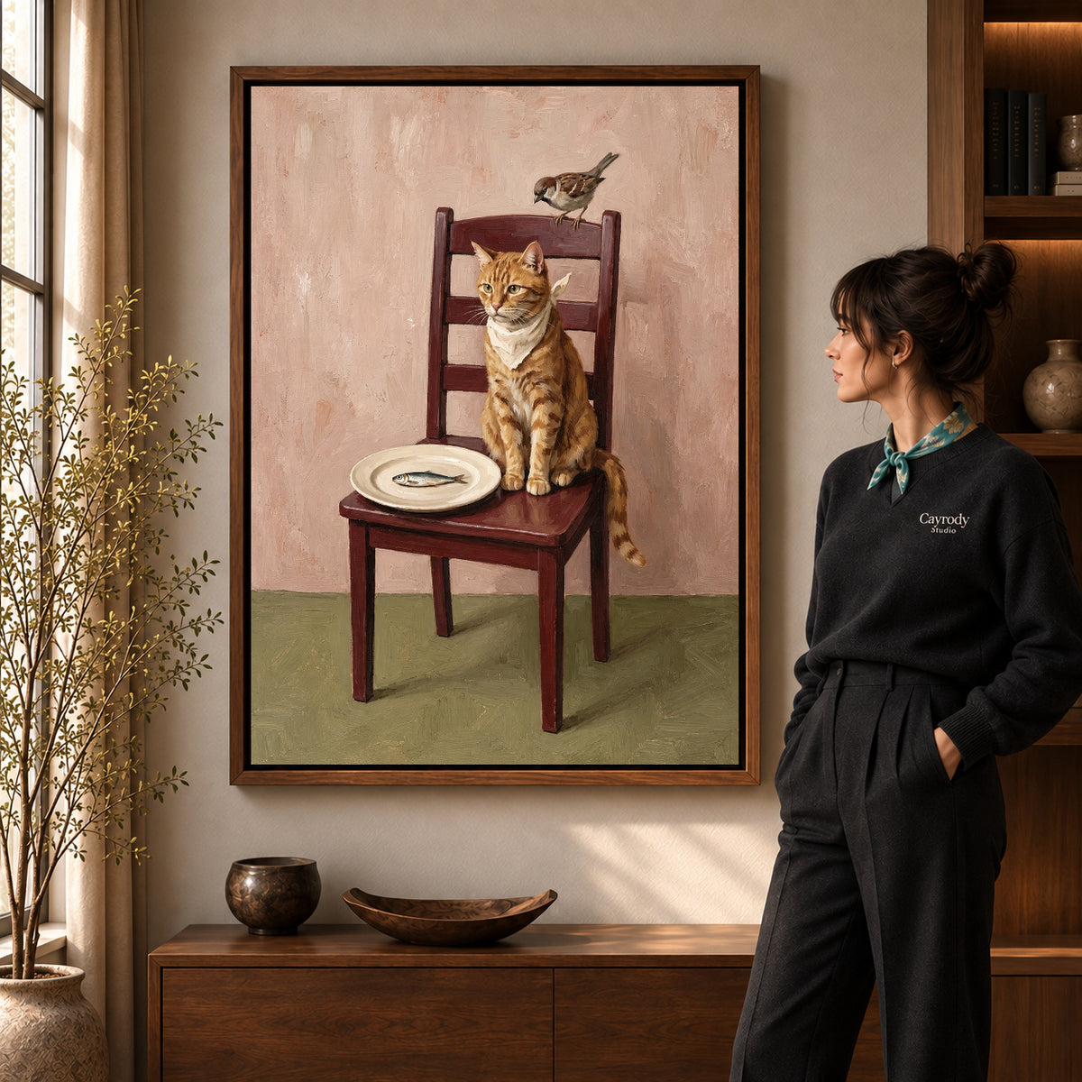 Cat and Sparrow artwork in a walnut frame beside a standing woman in a warm room.