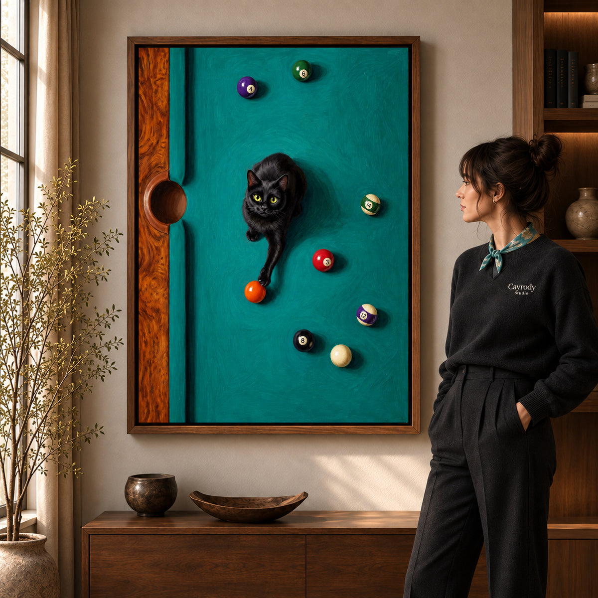 Playful Billiard Cat artwork in a walnut frame beside a standing woman in a warm room.