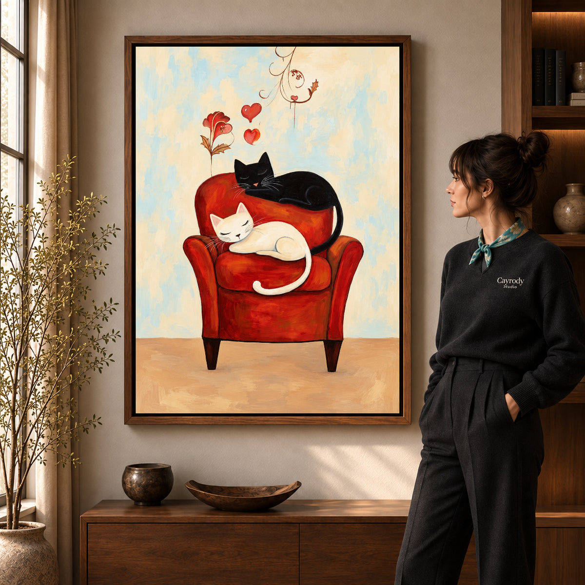 Sleeping Armchair Cats artwork in a walnut frame beside a standing woman in a warm room.
