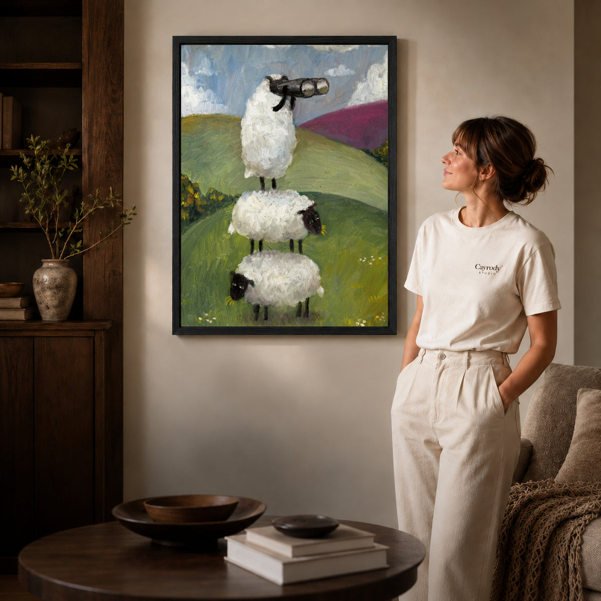 Black framed curious sheep stack artwork beside a woman in a warm neutral living room.