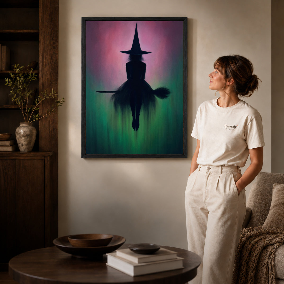 Black framed moody witch silhouette artwork beside a woman in a warm neutral living room.