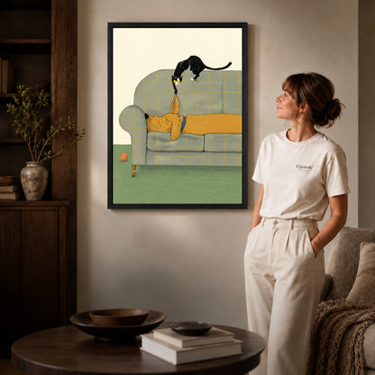Black framed mischievous sofa kitten artwork beside a woman in a warm neutral living room.