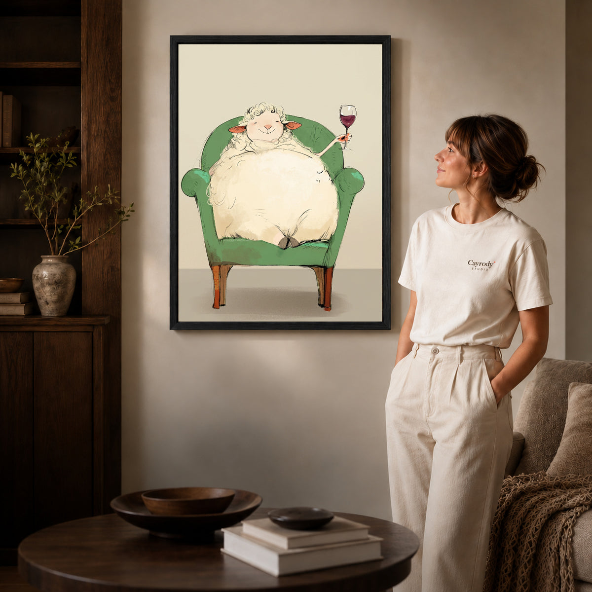 Black framed relaxed wine sheep artwork beside a woman in a warm neutral living room.
