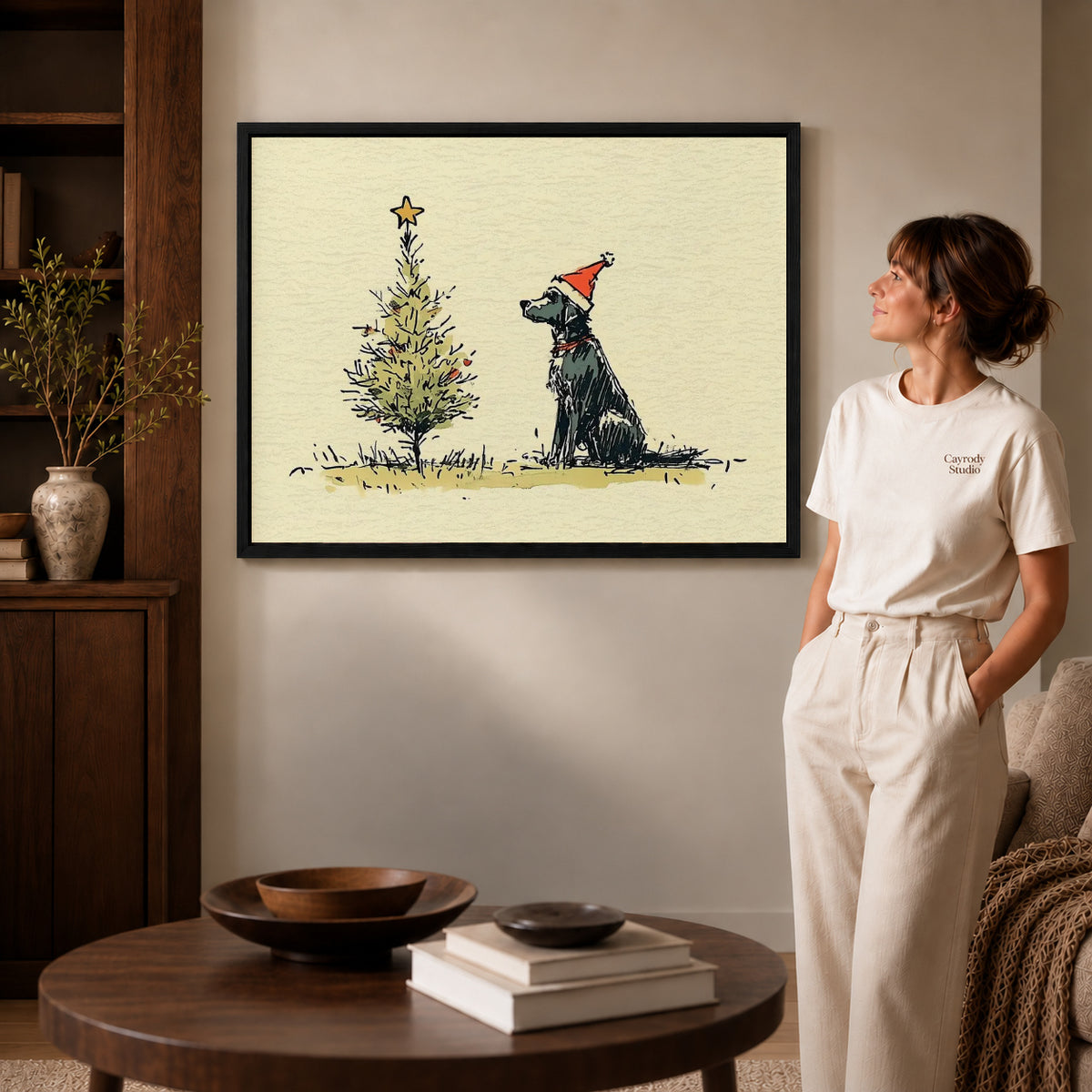 Black framed christmas dog sketch artwork beside a woman in a warm neutral living room.