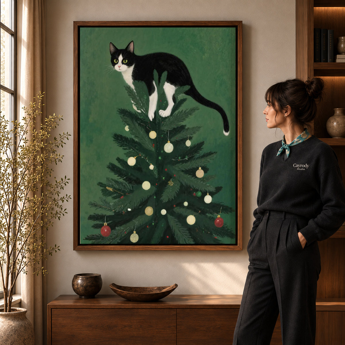 Christmas Tree Kitten artwork in a walnut frame beside a standing woman in a warm room.