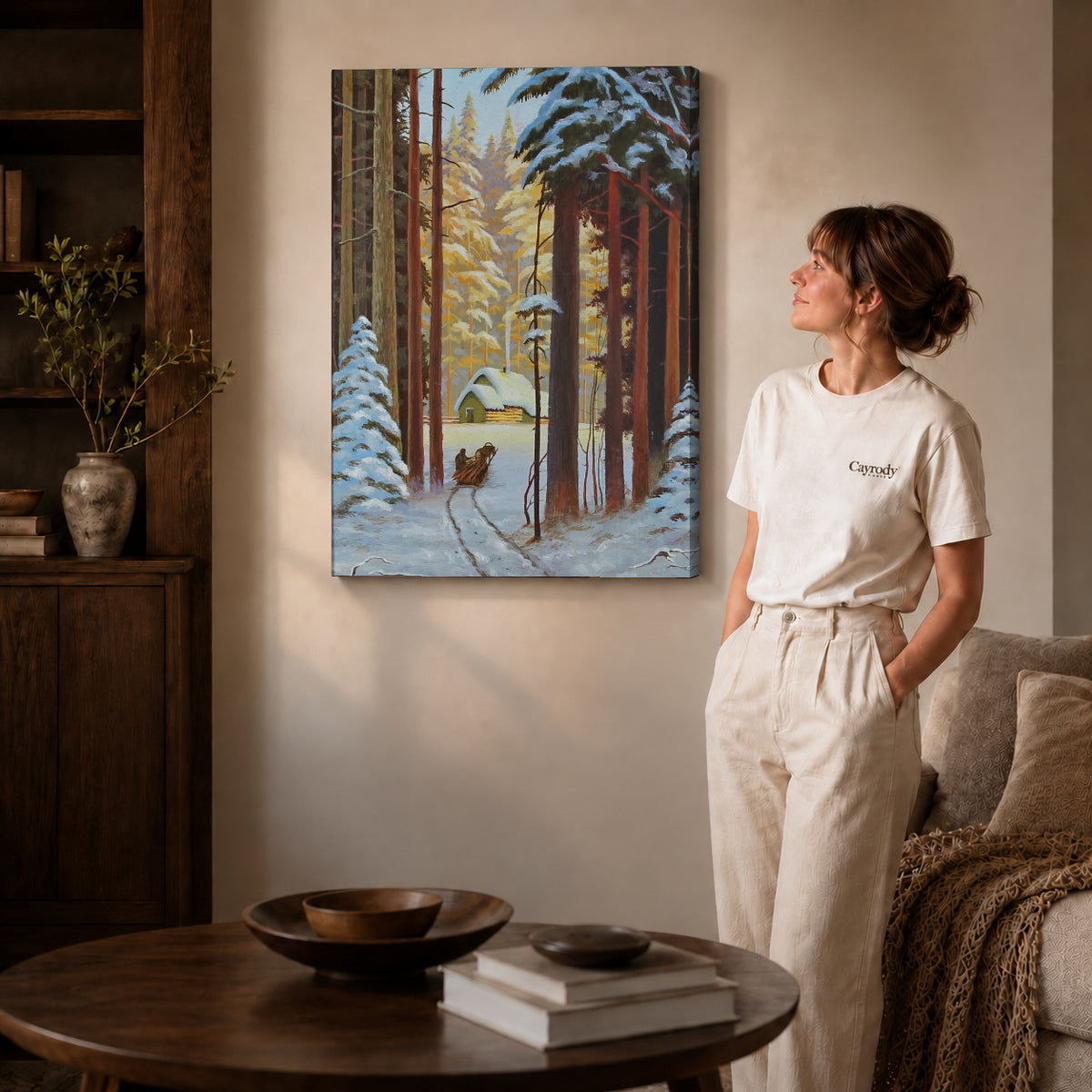 Gallery wrapped snowy forest sleigh artwork with shaded canvas edges beside a woman wearing cream clothing.