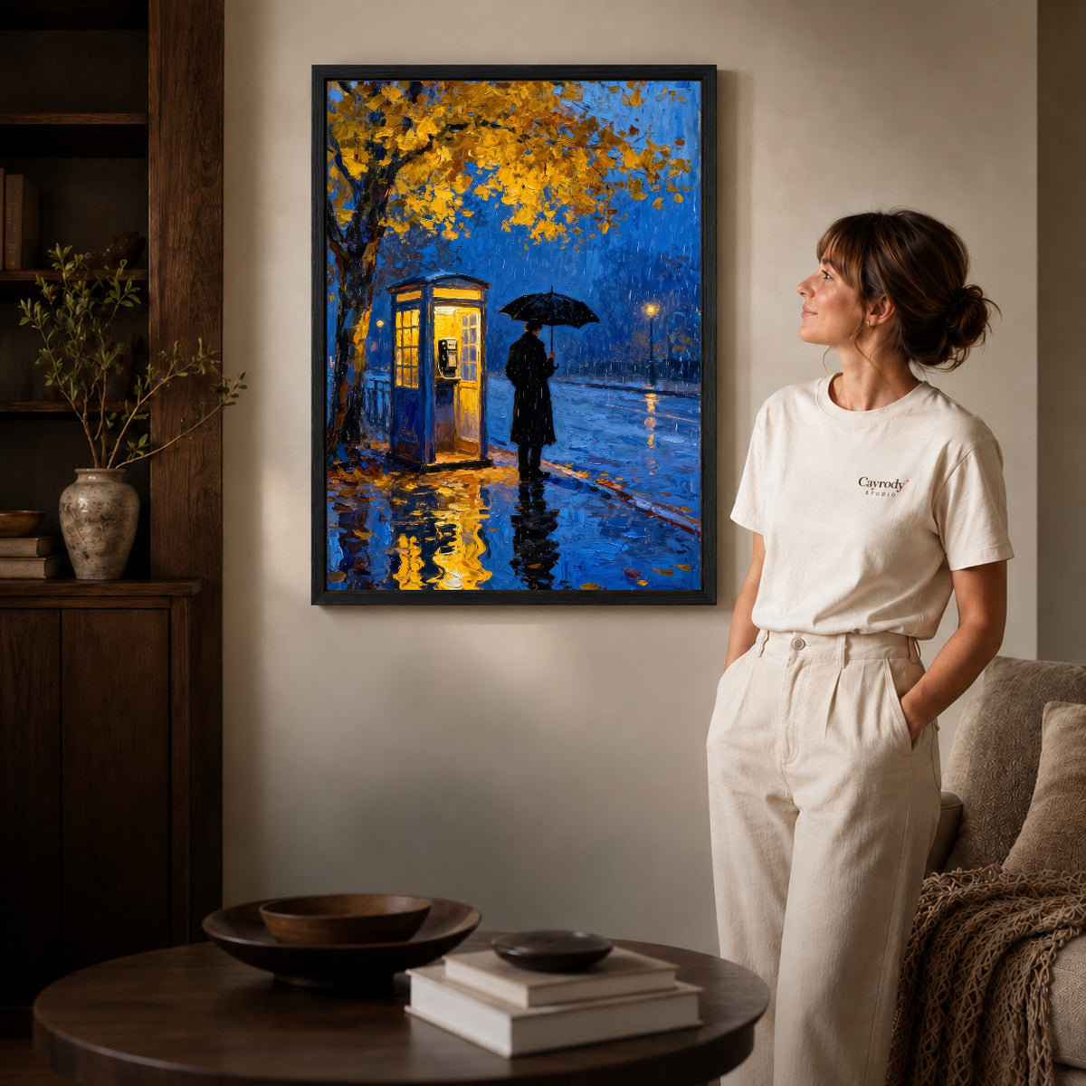 Black framed rainy blue telephone artwork beside a woman in a warm neutral living room.
