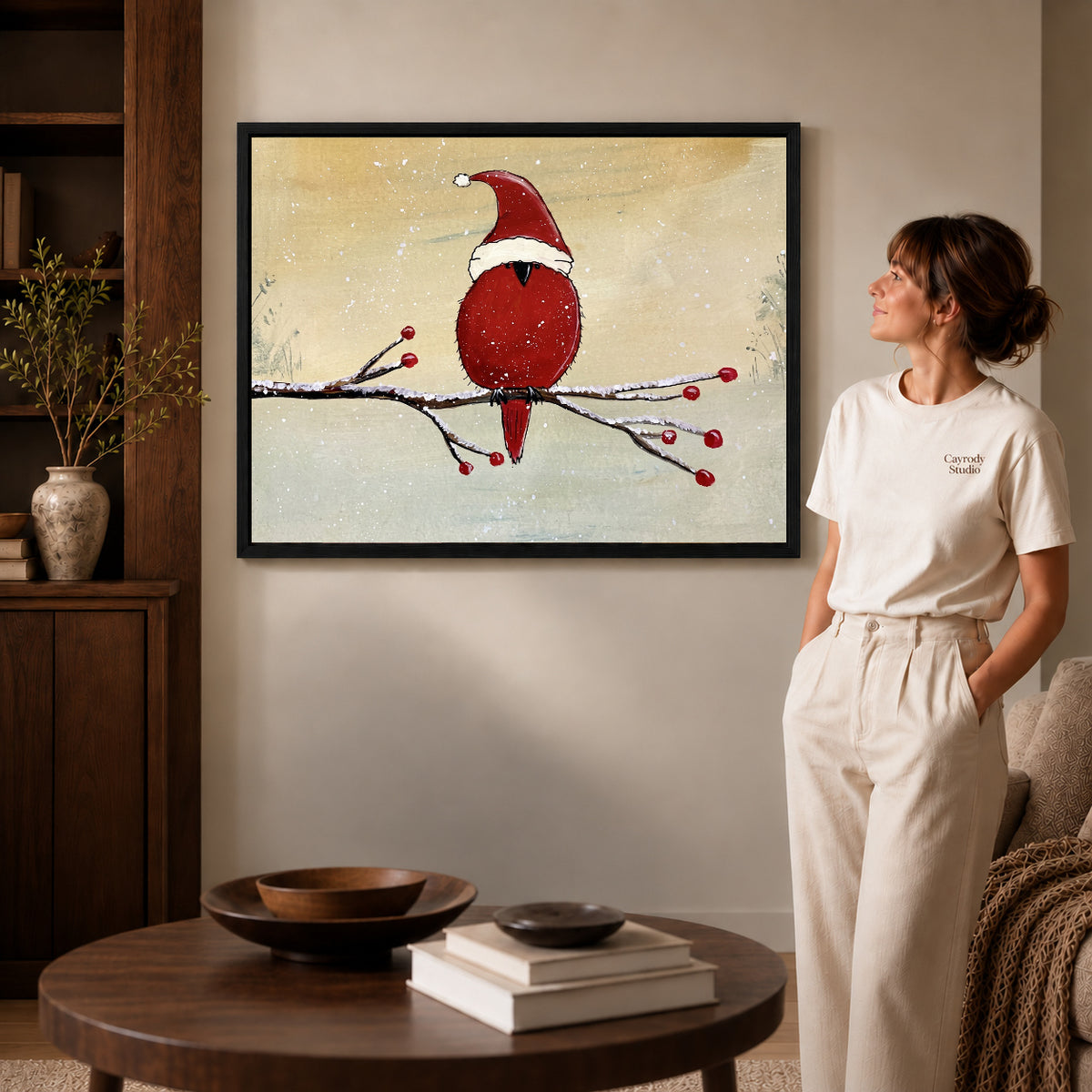 Black framed christmas cardinal artwork beside a woman in a warm neutral living room.