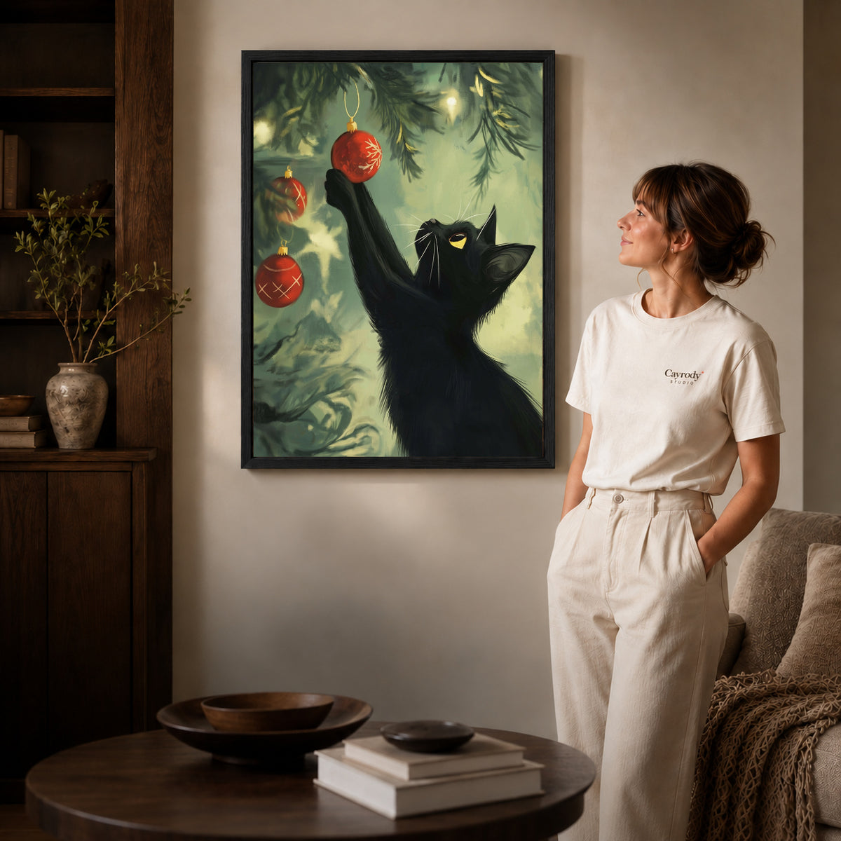 Black framed christmas bauble cat artwork beside a woman in a warm neutral living room.