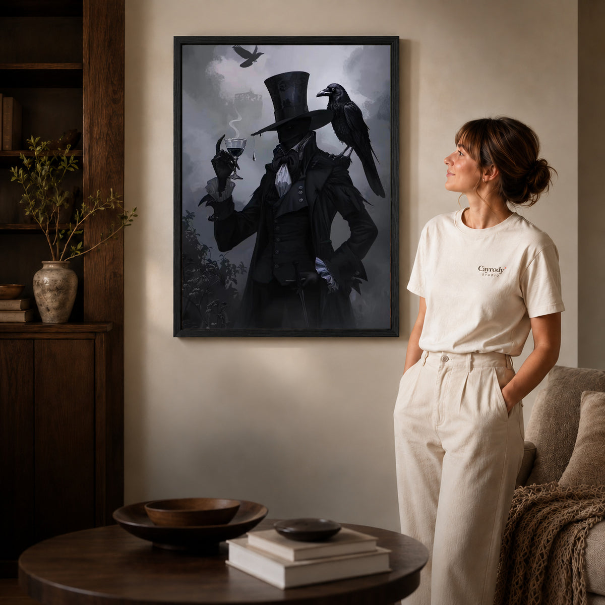 Black framed gothic raven gentleman artwork beside a woman in a warm neutral living room.