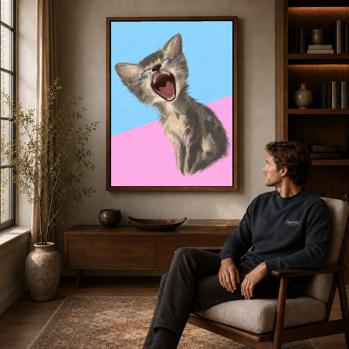 Walnut framed yawning kitten portrait artwork above a seated man in a wood furnished living room.