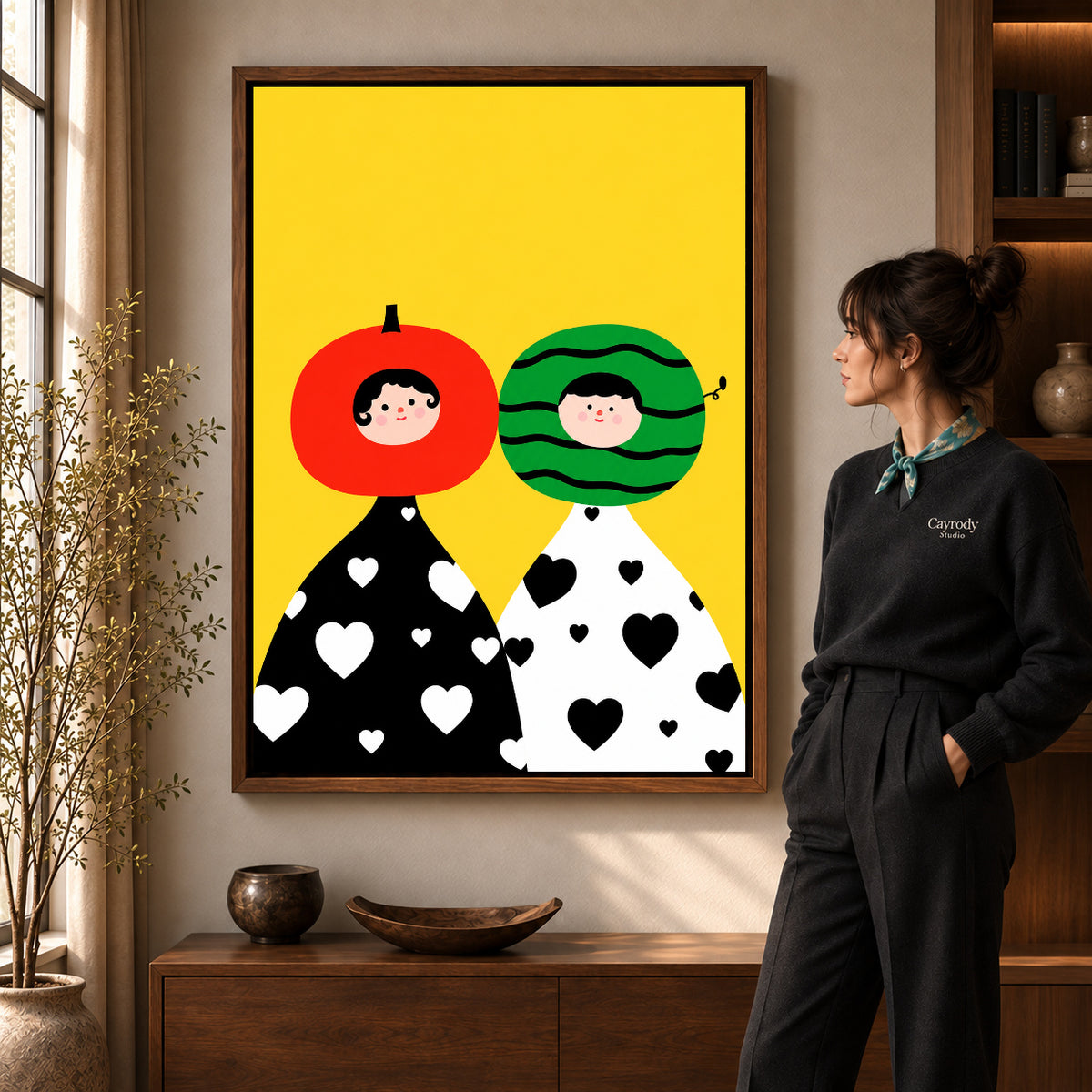 Fruit Head Couple artwork in a walnut frame beside a standing woman in a warm room.