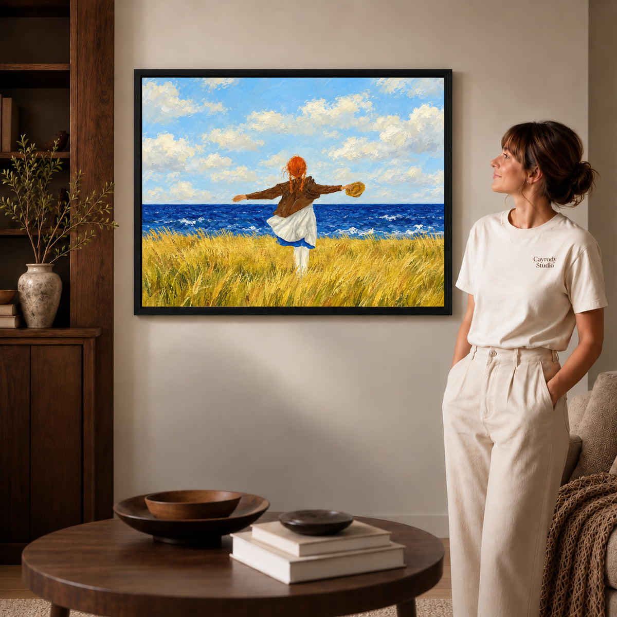 Black framed seaside freedom artwork beside a woman in a warm neutral living room.