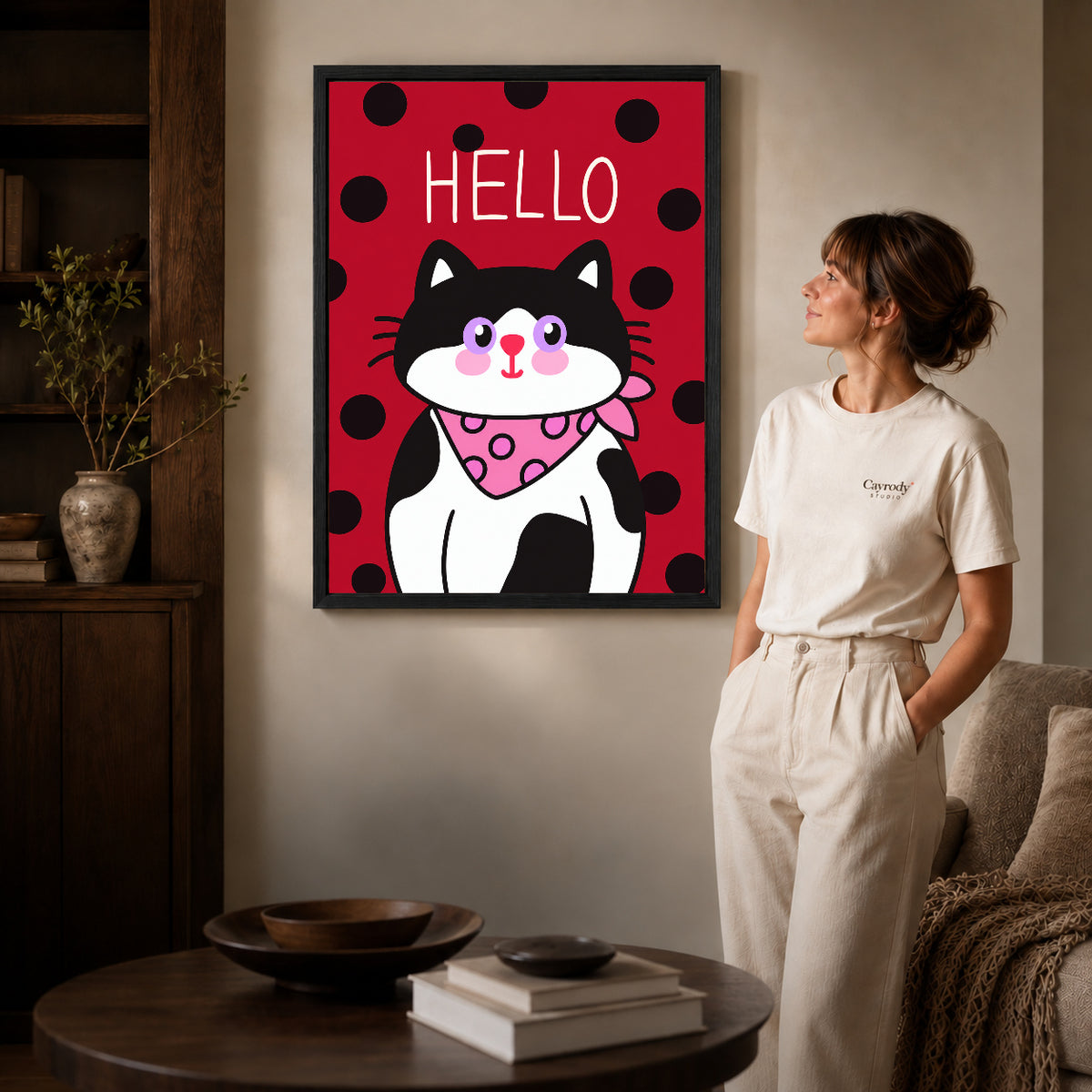 Black framed hello bandana cat artwork beside a woman in a warm neutral living room.