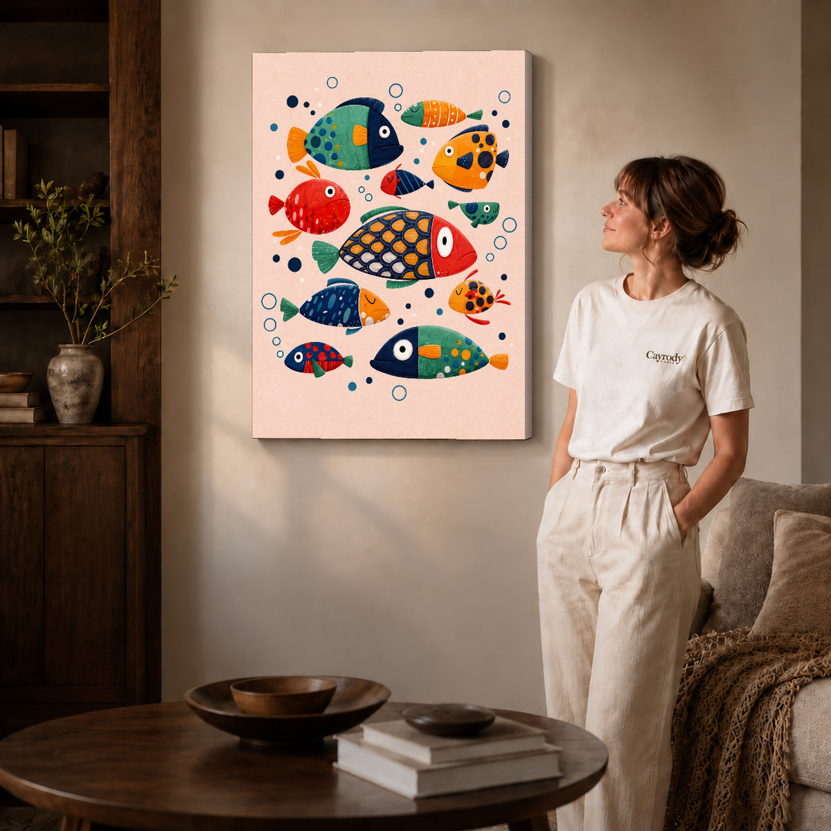 Gallery wrapped colorful folk fish artwork with shaded canvas edges beside a woman wearing cream clothing.