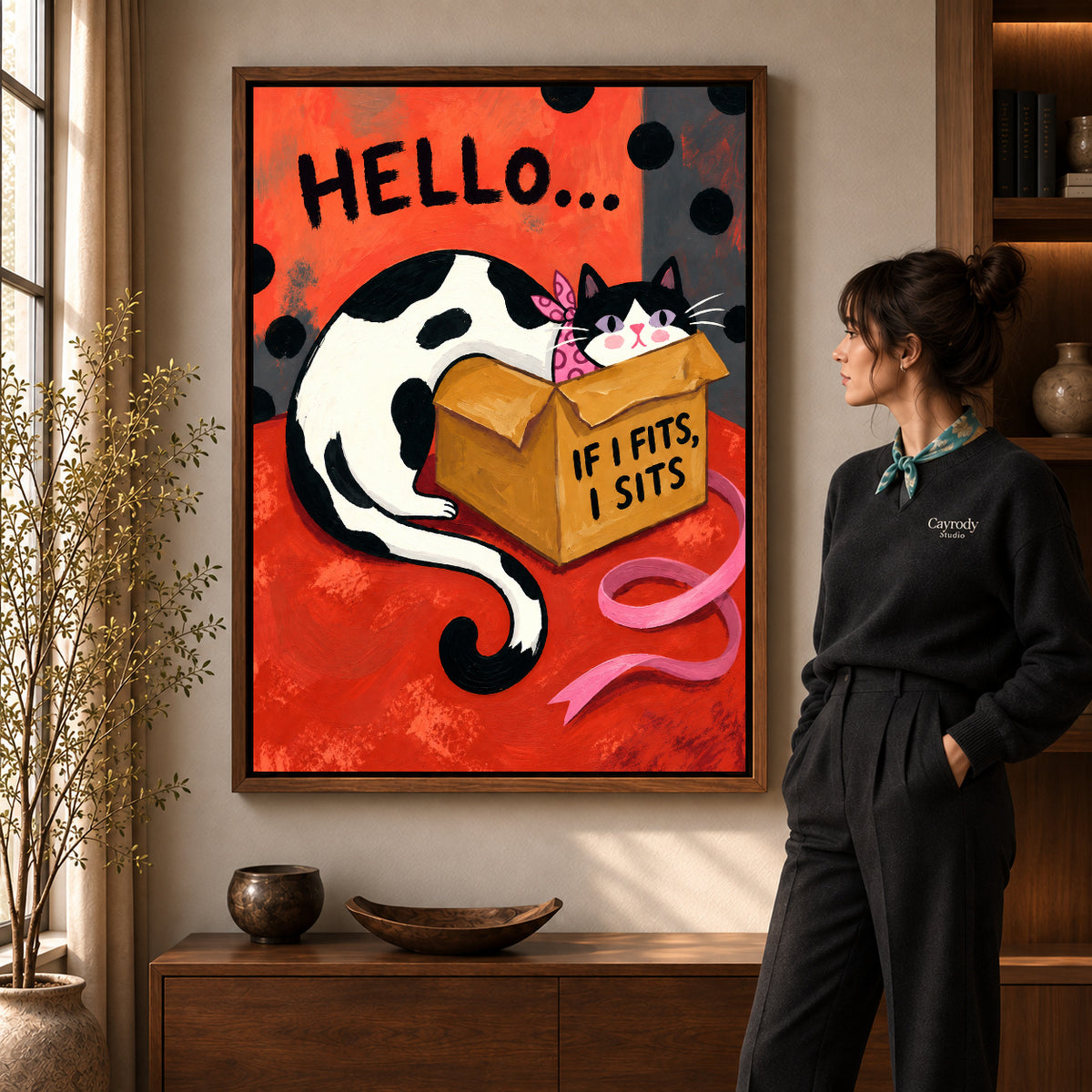 Cozy Cardboard Cat artwork in a walnut frame beside a standing woman in a warm room.