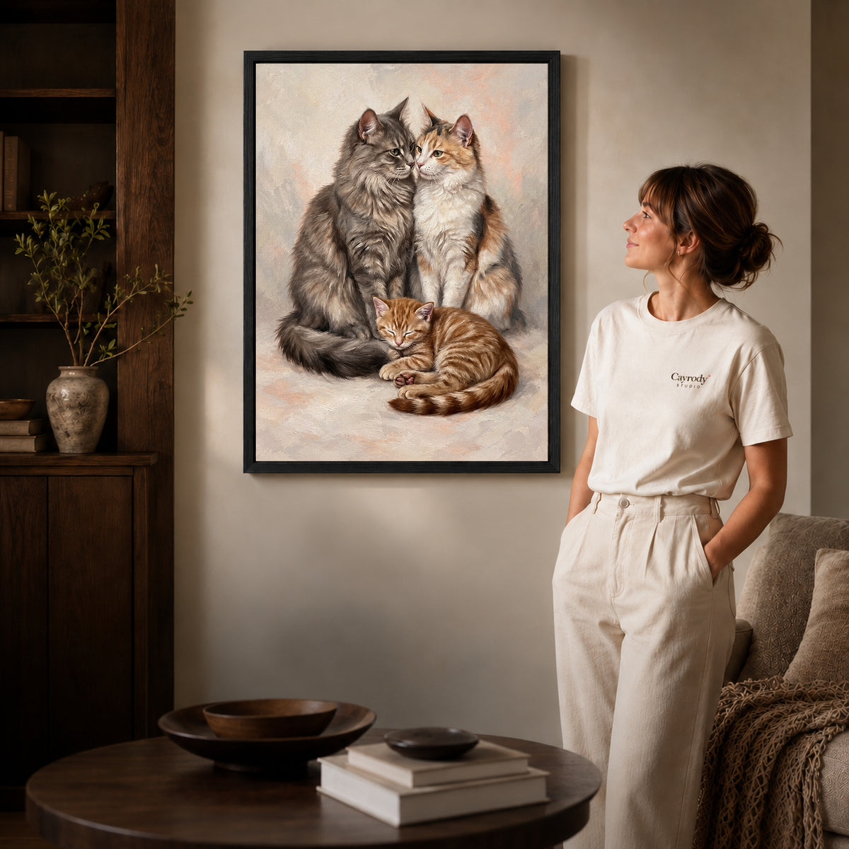Black framed gentle cat family artwork beside a woman in a warm neutral living room.