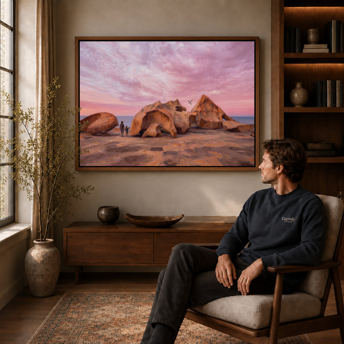 Walnut framed coastal rock sunset artwork above a seated man in a wood furnished living room.
