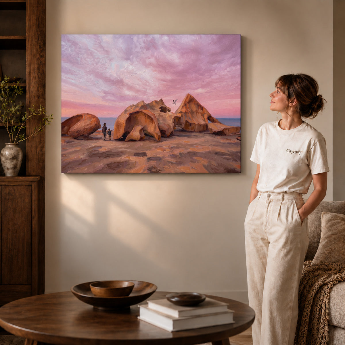 Gallery wrapped coastal rock sunset artwork with shaded canvas edges beside a woman wearing cream clothing.