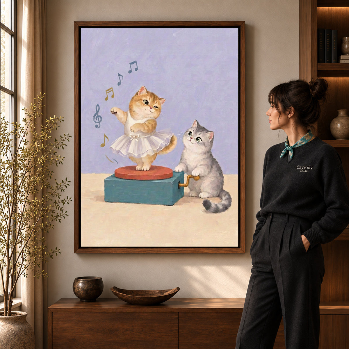 Music Box Kittens artwork in a walnut frame beside a standing woman in a warm room.