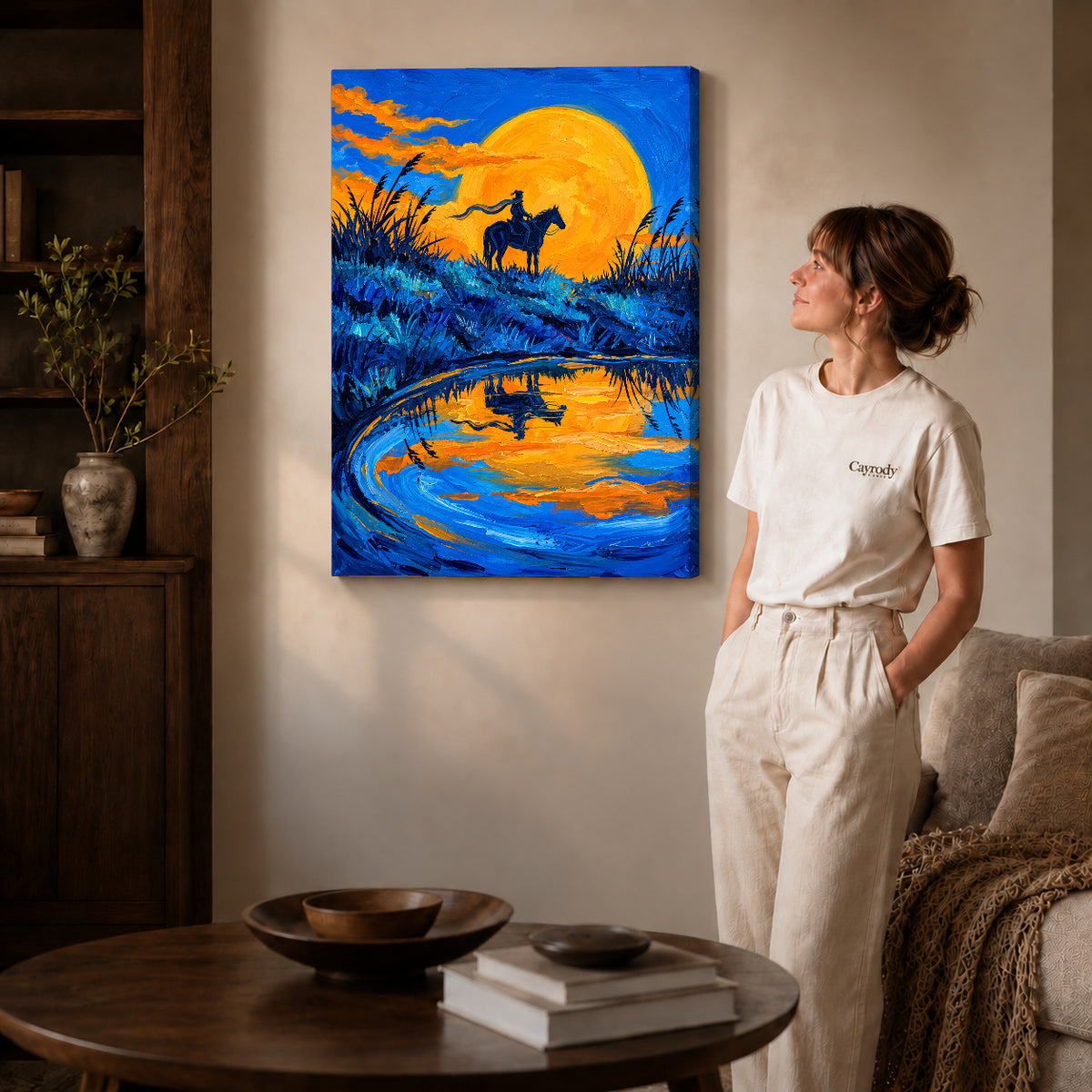 Gallery wrapped golden moon rider artwork with shaded canvas edges beside a woman wearing cream clothing.