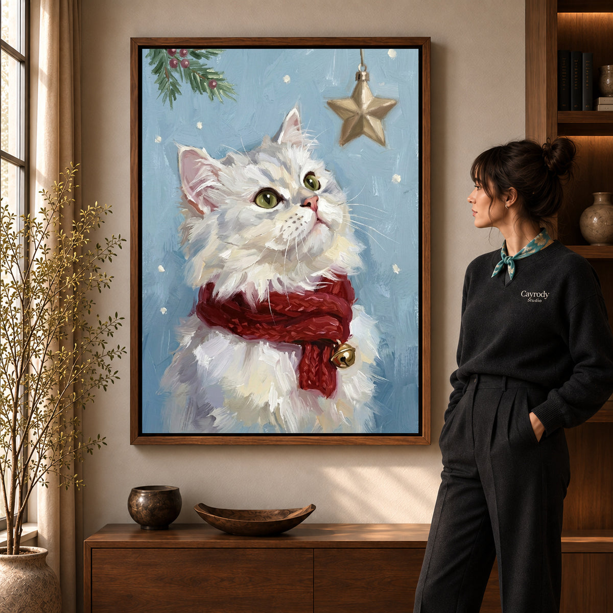 Christmas Star Kitten artwork in a walnut frame beside a standing woman in a warm room.
