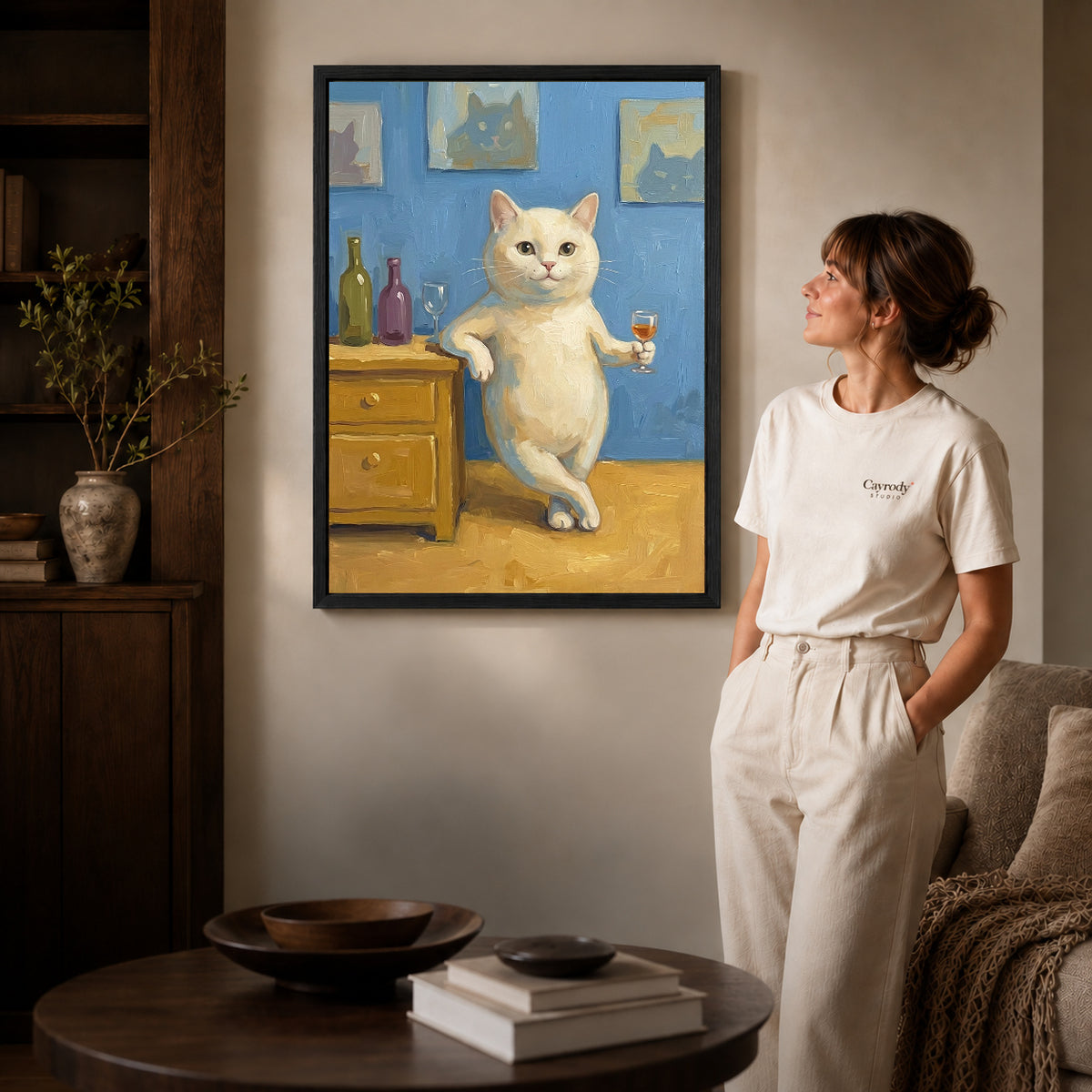 Black framed relaxed wine cat artwork beside a woman in a warm neutral living room.
