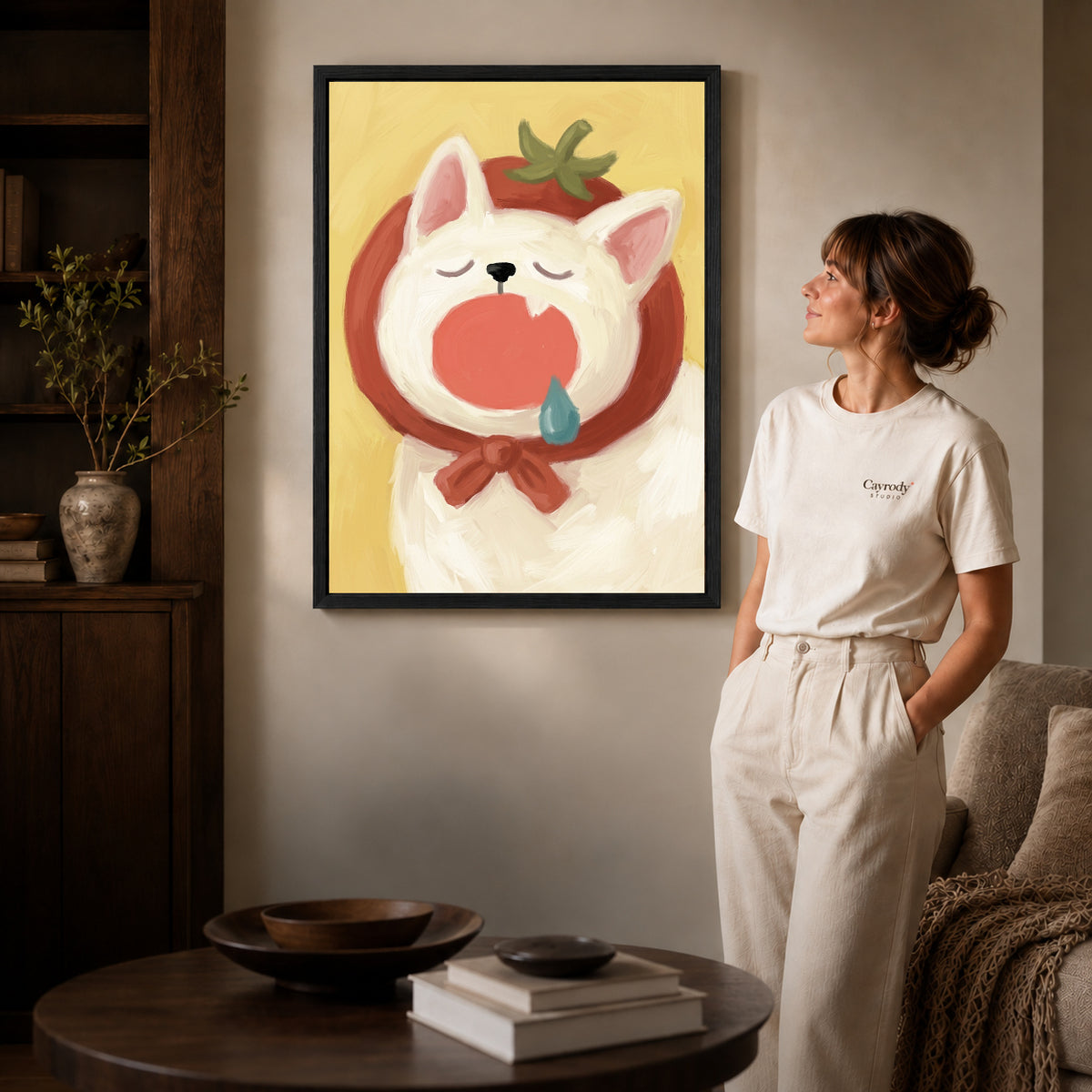 Black framed yawning hood cat artwork beside a woman in a warm neutral living room.