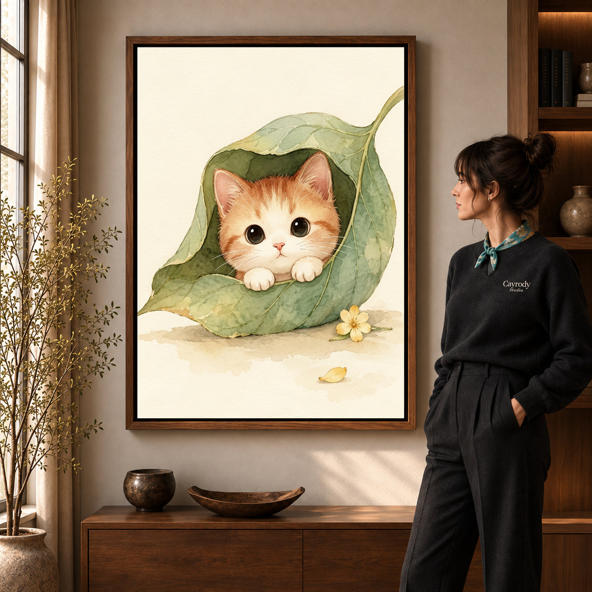 Leaf Pocket Kitten artwork in a walnut frame beside a standing woman in a warm room.