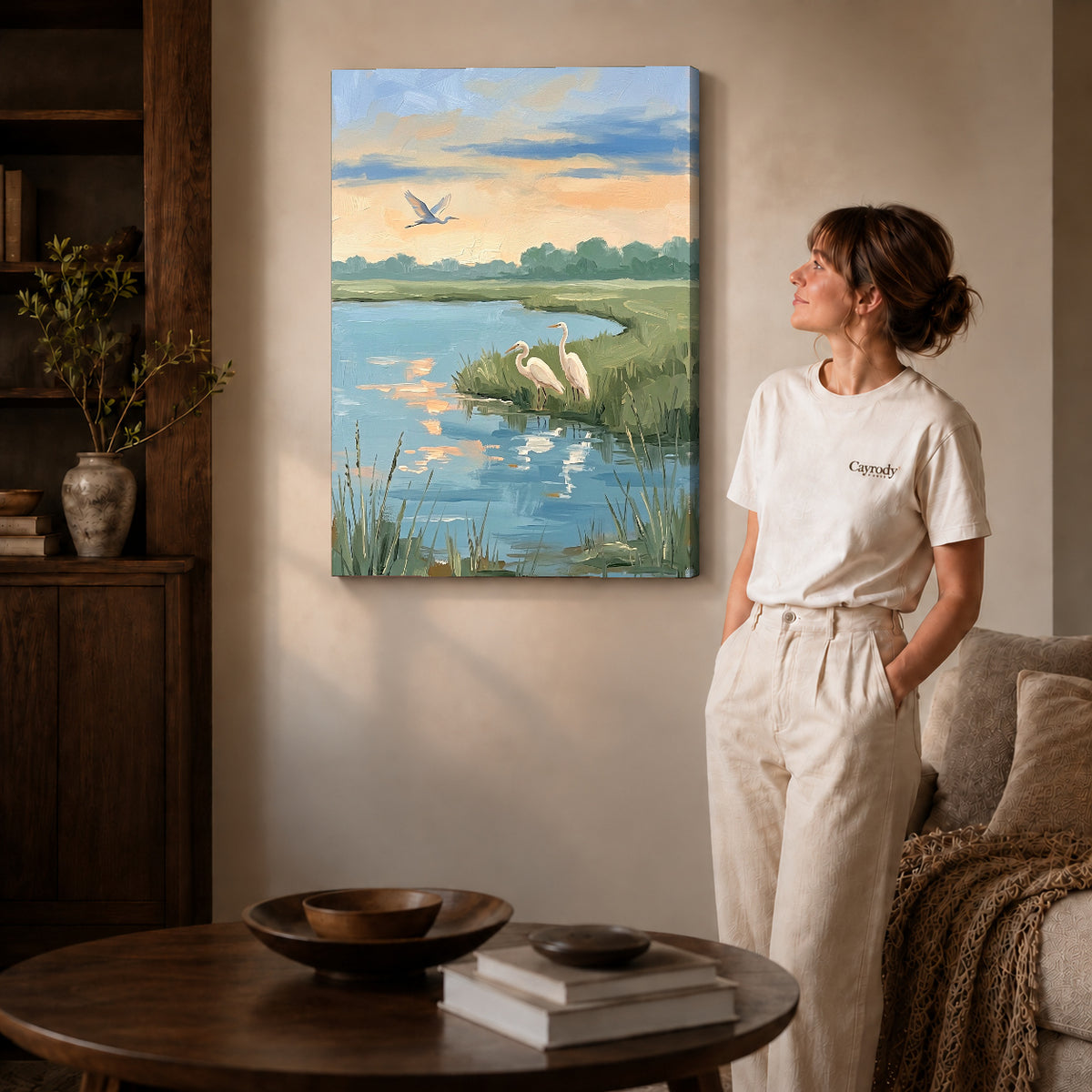 Gallery wrapped quiet marsh herons artwork with shaded canvas edges beside a woman wearing cream clothing.