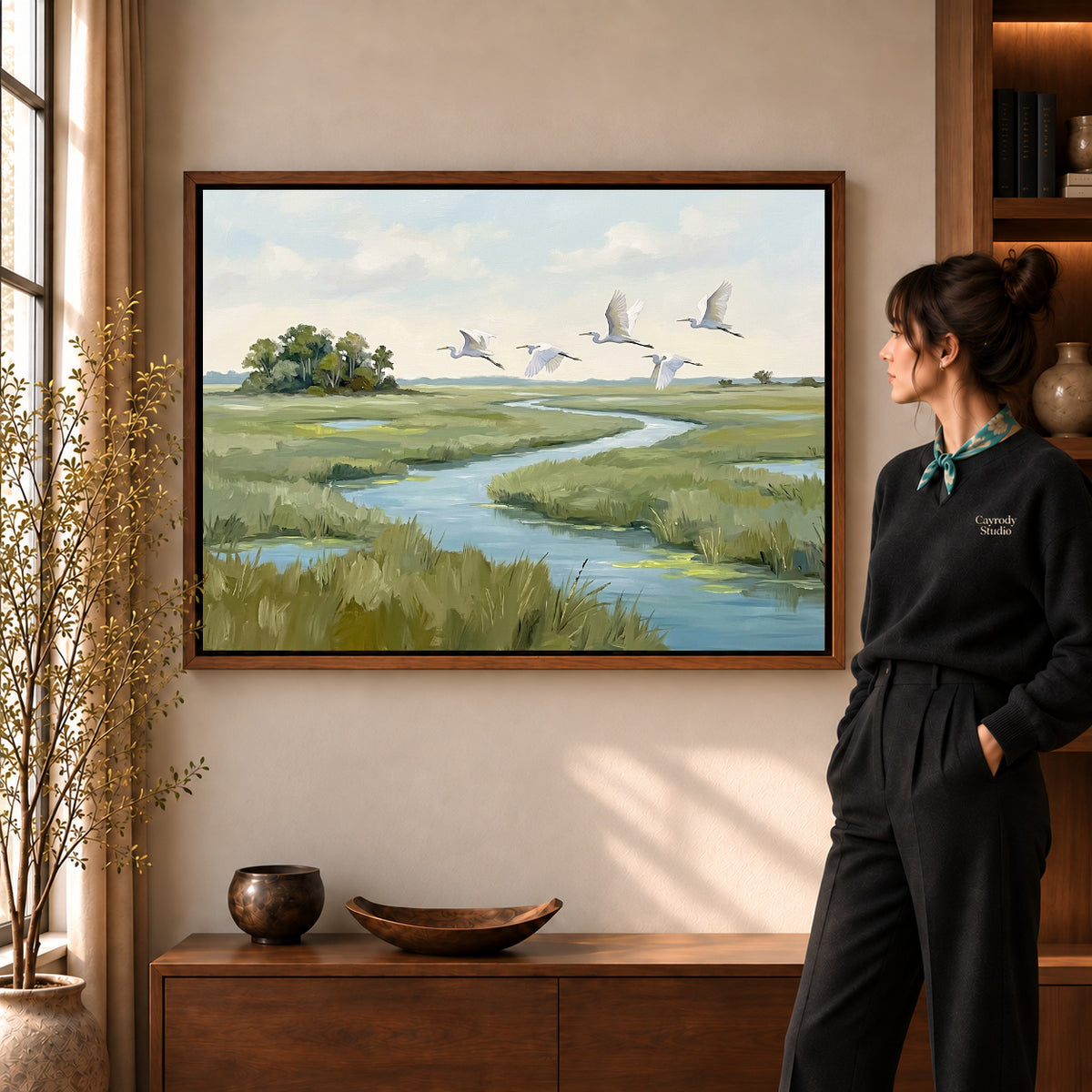 Marsh Bird Flight artwork in a walnut frame beside a standing woman in a warm room.