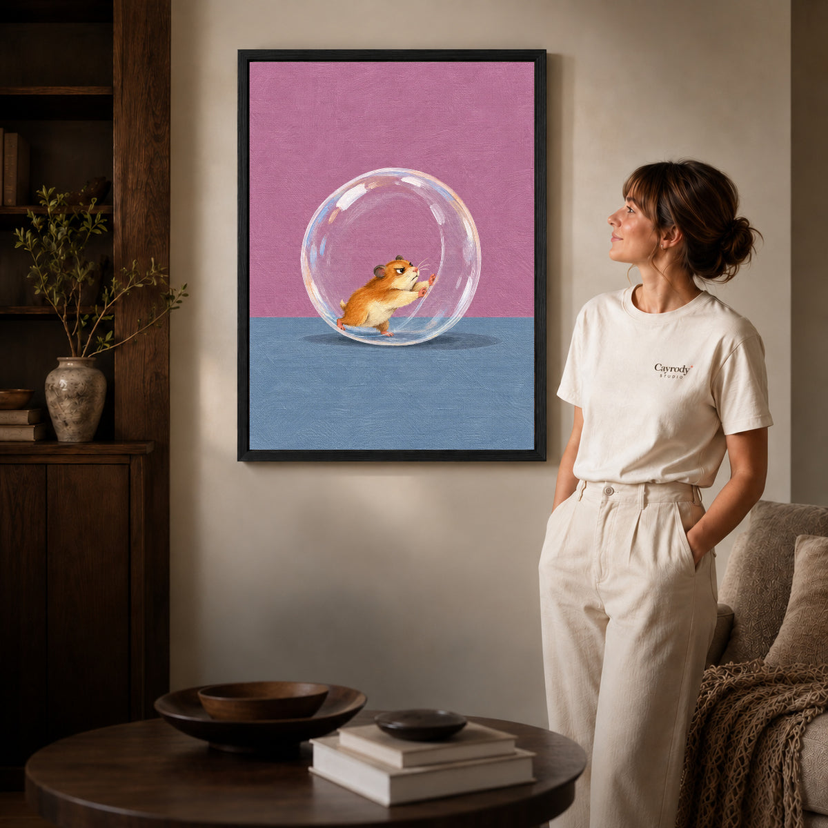 Black framed determined hamster runner artwork beside a woman in a warm neutral living room.
