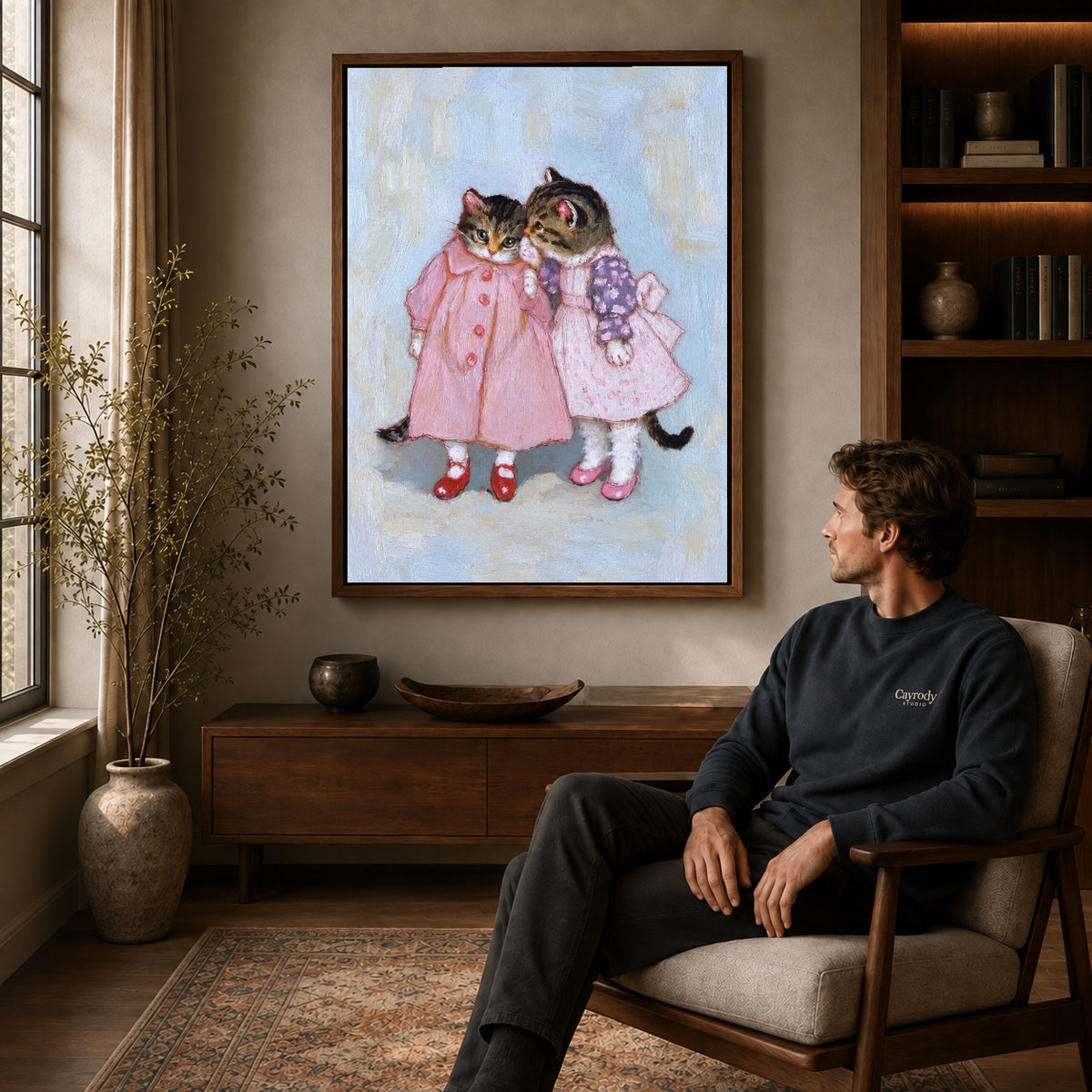 Walnut framed pink dress kitten friends artwork above a seated man in a wood furnished living room.