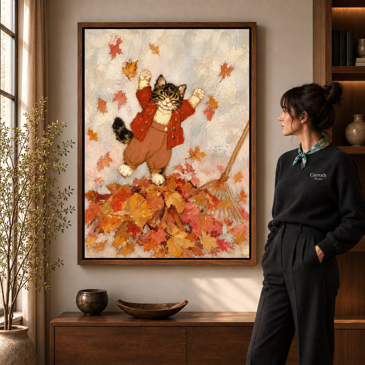 Autumn Leaf Kitten artwork in a walnut frame beside a standing woman in a warm room.