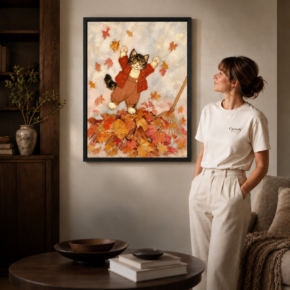 Black framed autumn leaf kitten artwork beside a woman in a warm neutral living room.