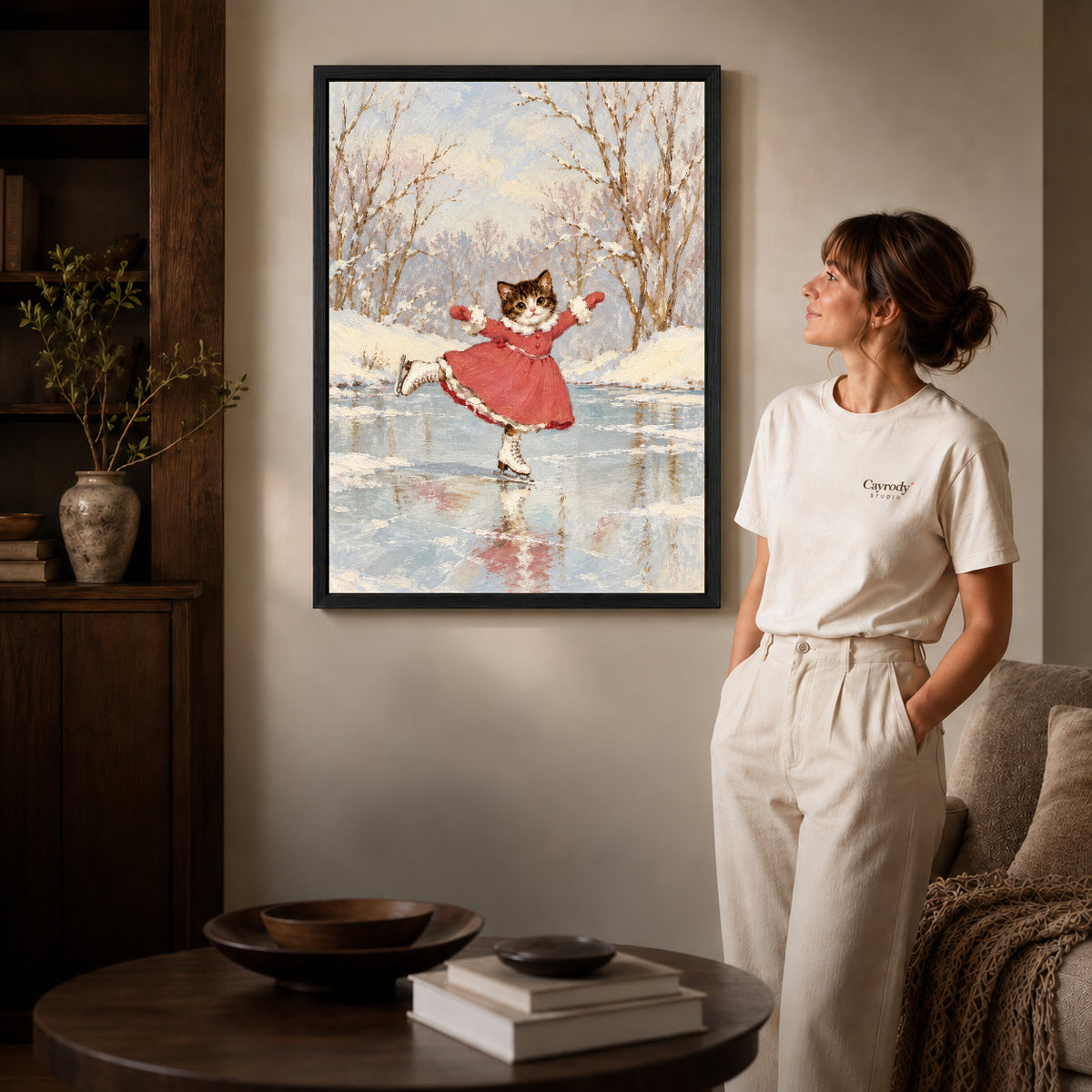 Black framed winter skating kitten artwork beside a woman in a warm neutral living room.