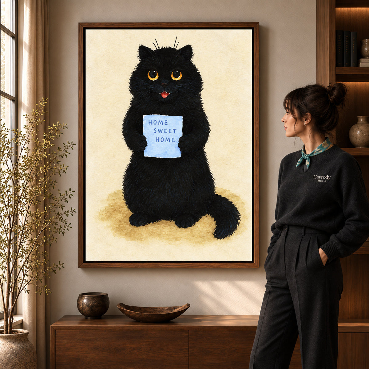 Home Sweet Cat artwork in a walnut frame beside a standing woman in a warm room.