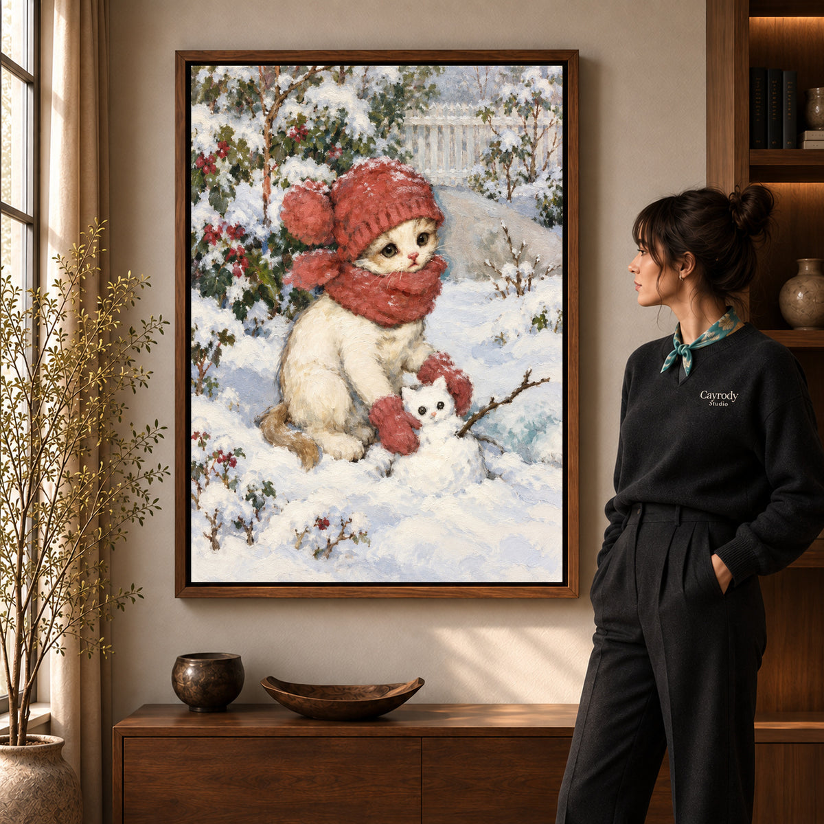 Snowman Kitten Friend artwork in a walnut frame beside a standing woman in a warm room.
