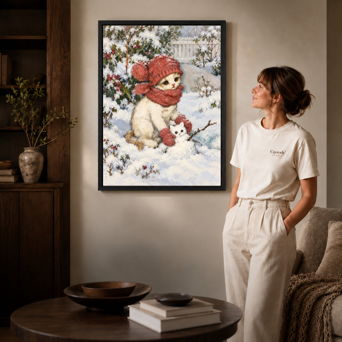 Black framed snowman kitten friend artwork beside a woman in a warm neutral living room.