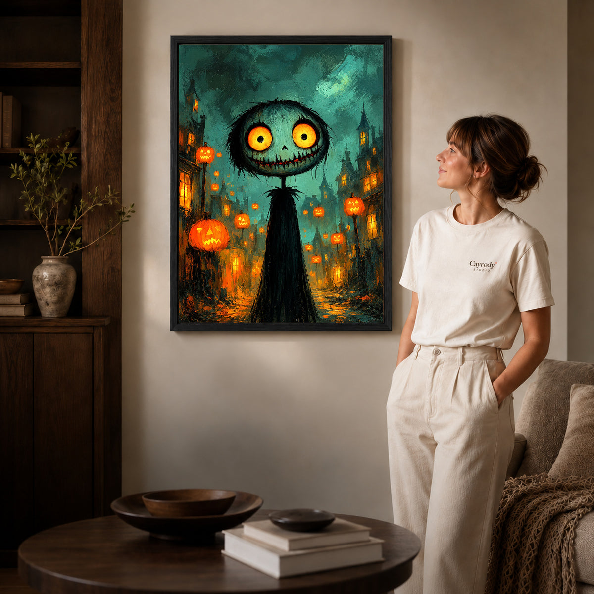 Black framed glowing halloween creature artwork beside a woman in a warm neutral living room.
