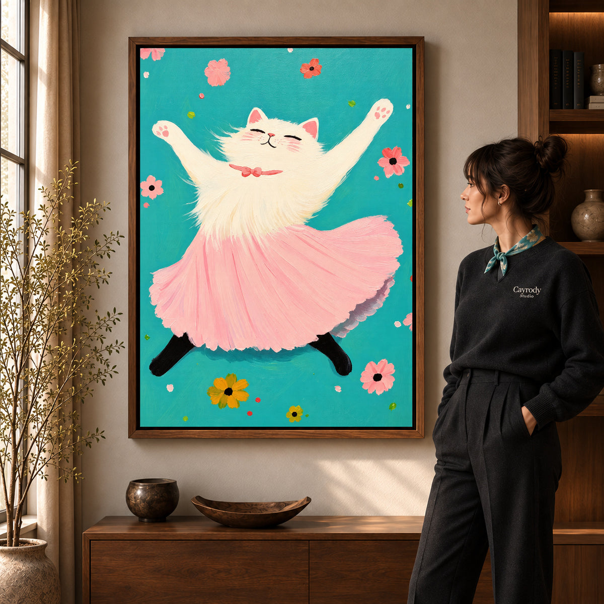 Joyful Ballet Cat artwork in a walnut frame beside a standing woman in a warm room.