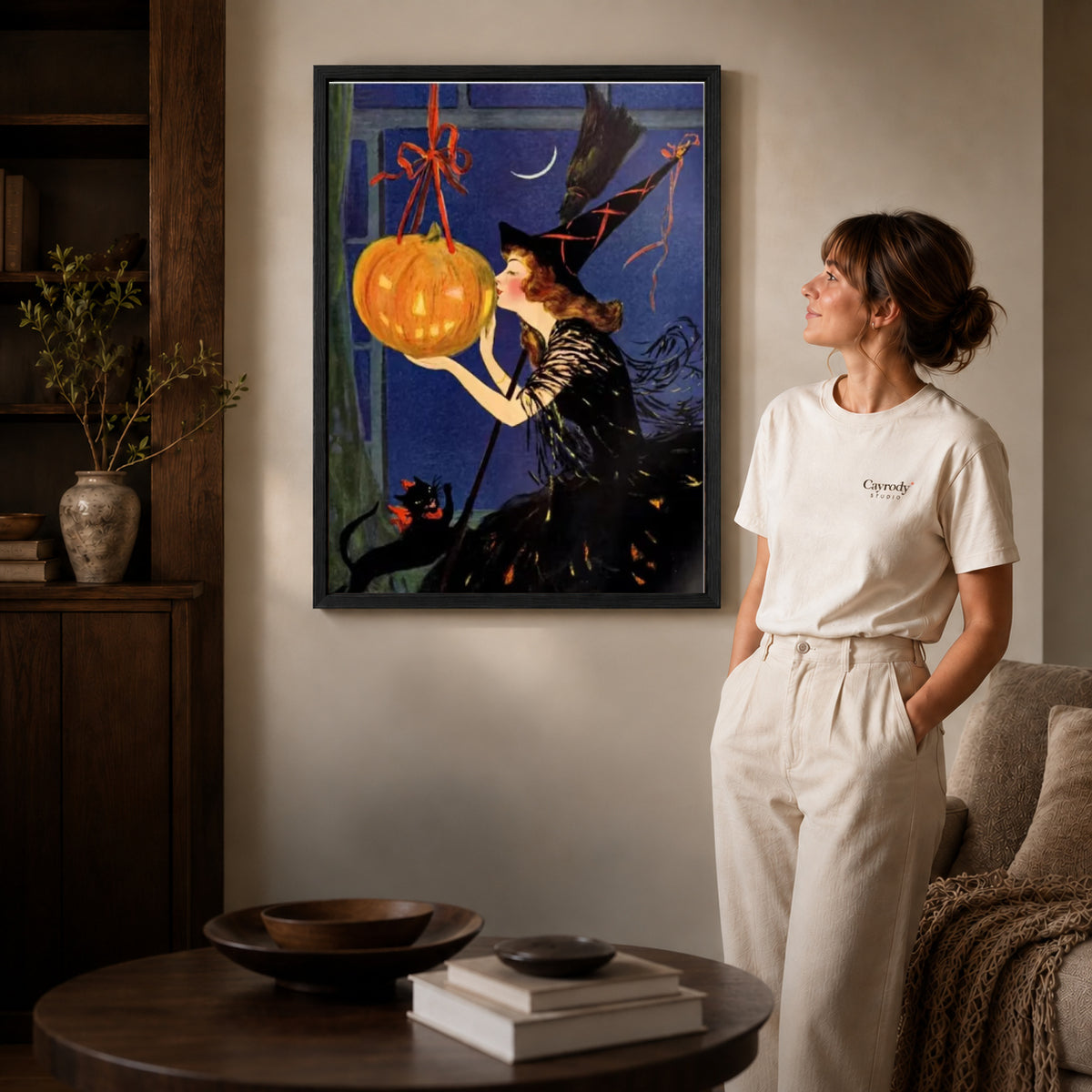 Black framed vintage witch canvas art displayed beside a woman in a warm neutral living room.