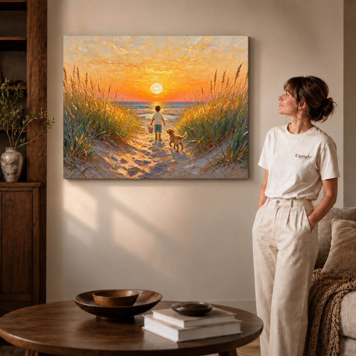 Gallery wrapped sunset beach companions artwork with shaded canvas edges beside a woman wearing cream clothing.