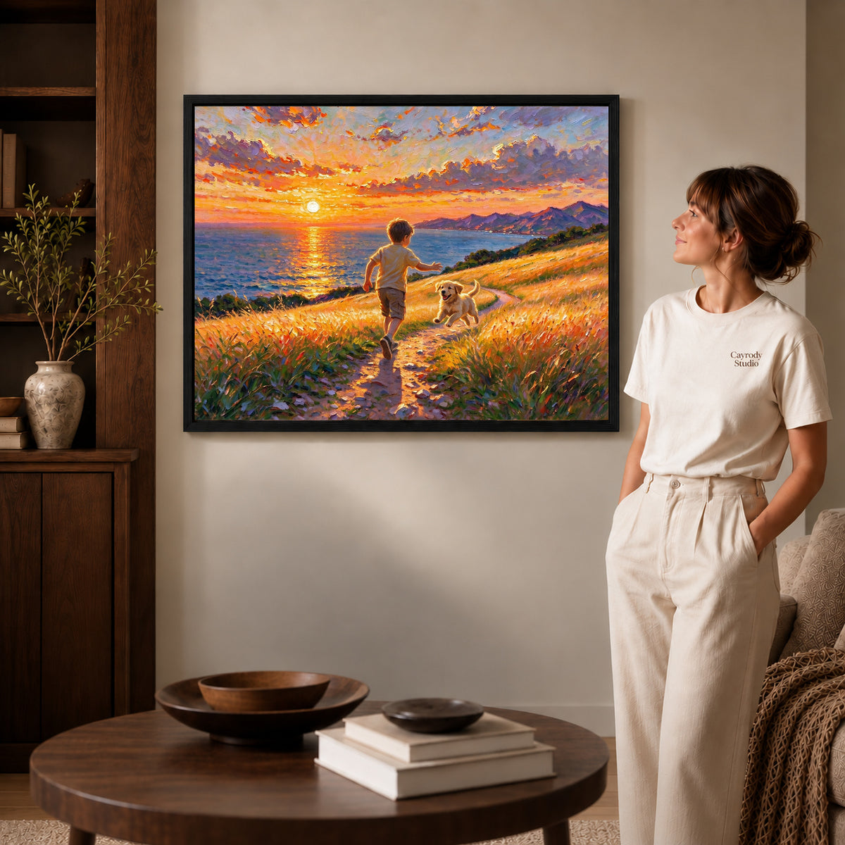 Black framed golden coastal run artwork beside a woman in a warm neutral living room.