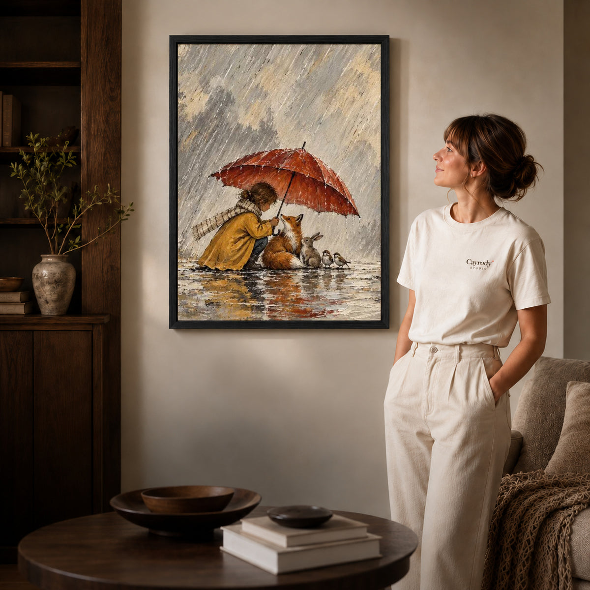 Black framed rainy woodland shelter artwork beside a woman in a warm neutral living room.