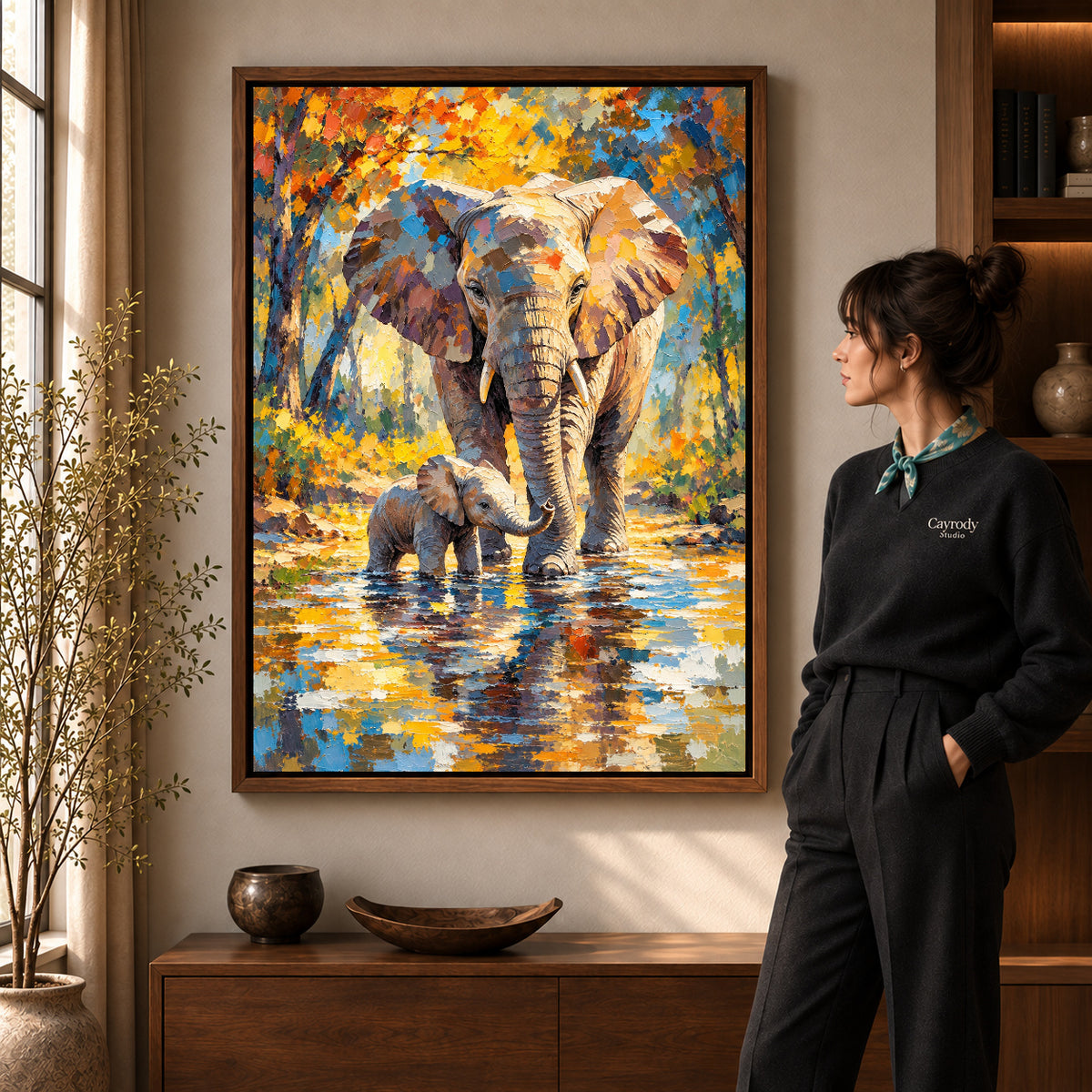 Elephant Family River artwork in a walnut frame beside a standing woman in a warm room.