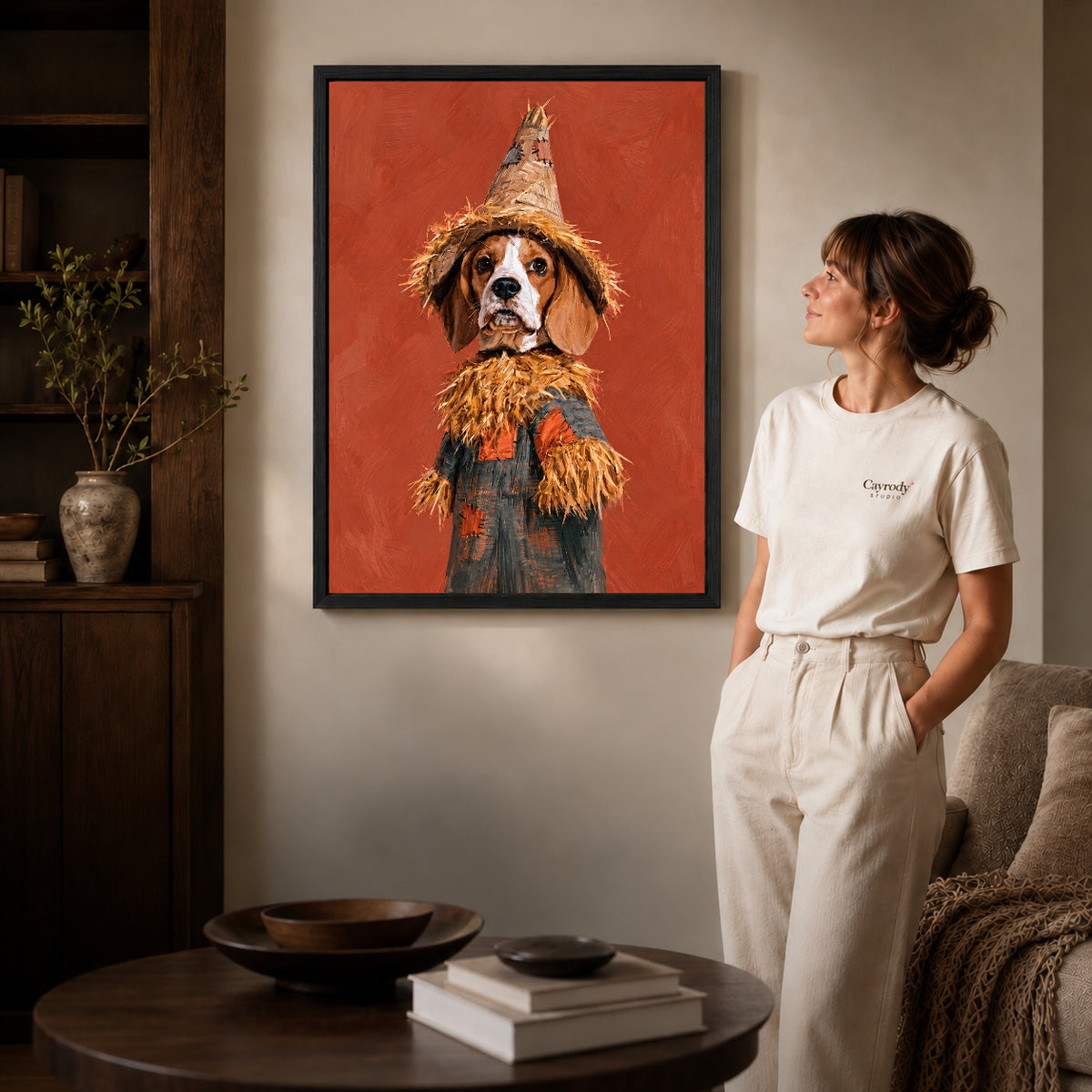 Black framed scarecrow spaniel artwork beside a woman in a warm neutral living room.