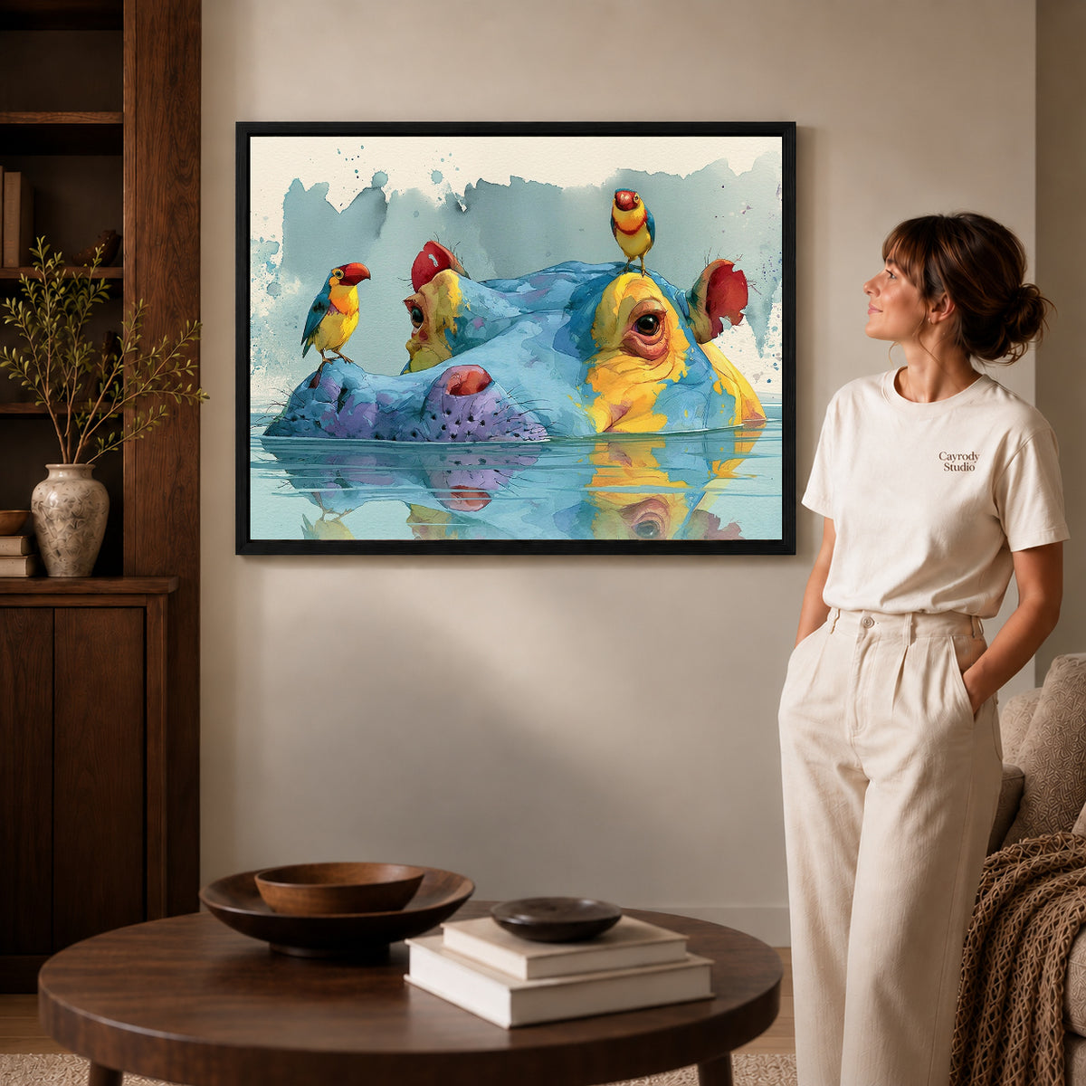 Black framed hippo bird friends artwork beside a woman in a warm neutral living room.